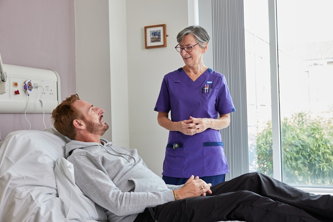 A photo of a matron standing next to a patient in a bed,