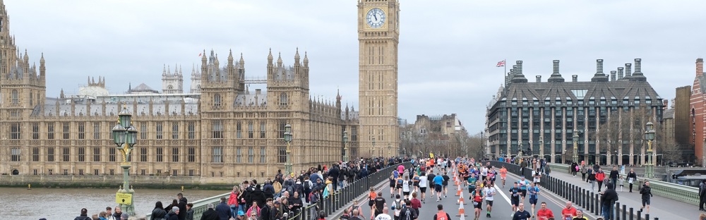 A photo of a running event in front of the Houses of Parliament in London with a group of runners running over the bridge.