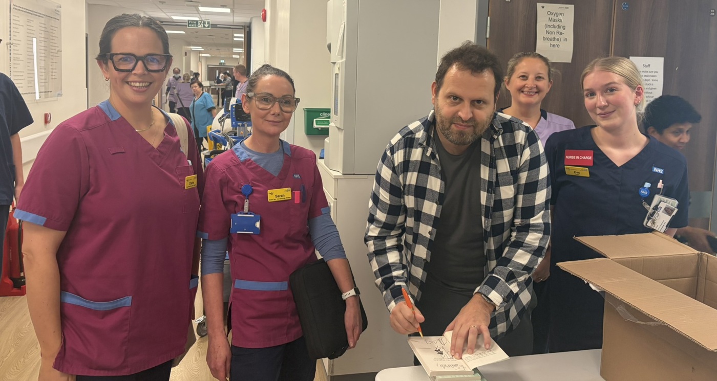 A photo of bestselling author and former doctor Adam Kay visiting a ward at The Christie and signing books for staff.