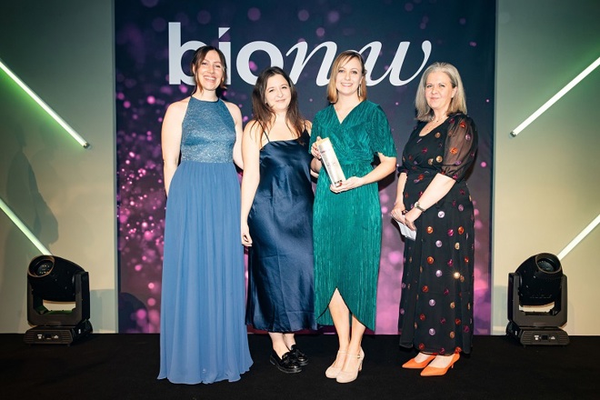 A photo of 4 female members of the Experimental Cancer Medicine Team at The Christie accepting their Bionow 2023 Social Impact Award at the Bionow Awards ceremony, with a purple background reading Bionow.