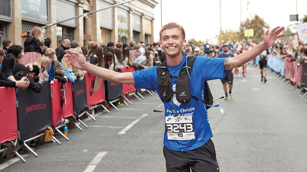 A photo of a man running in a Christie Charity t-shirt with his hands in the air.